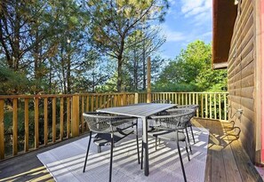 An outdoor deck with a table and chairs, surrounded by a wooden railing and trees. - Game Loft | Hot Tub | Fire Pit | Wooded Escape (Broken Bow)