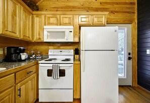 A kitchen with wooden cabinets, a white stove, a microwave, and a refrigerator. - Game Loft | Hot Tub | Fire Pit | Wooded Escape (Broken Bow)