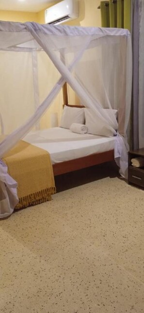 Een bed met hemel, een nachtkastje en een wandairconditioner.
