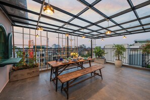 A rooftop terrace with a wooden table and benches, surrounded by potted plants and hanging lights. - Tranquility Suites Westlake (Hanoi)