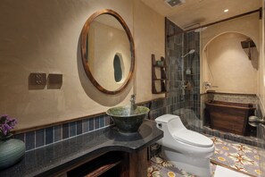 A bathroom with a large oval mirror, a sink with a green basin, a toilet, and a shower area with a glass door. - Tranquility Suites Westlake (Hanoi)