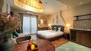 Una habitación de hotel con una cama, una mesa de comedor con frutas, una zona de cocina y un ventanal con cortinas.
