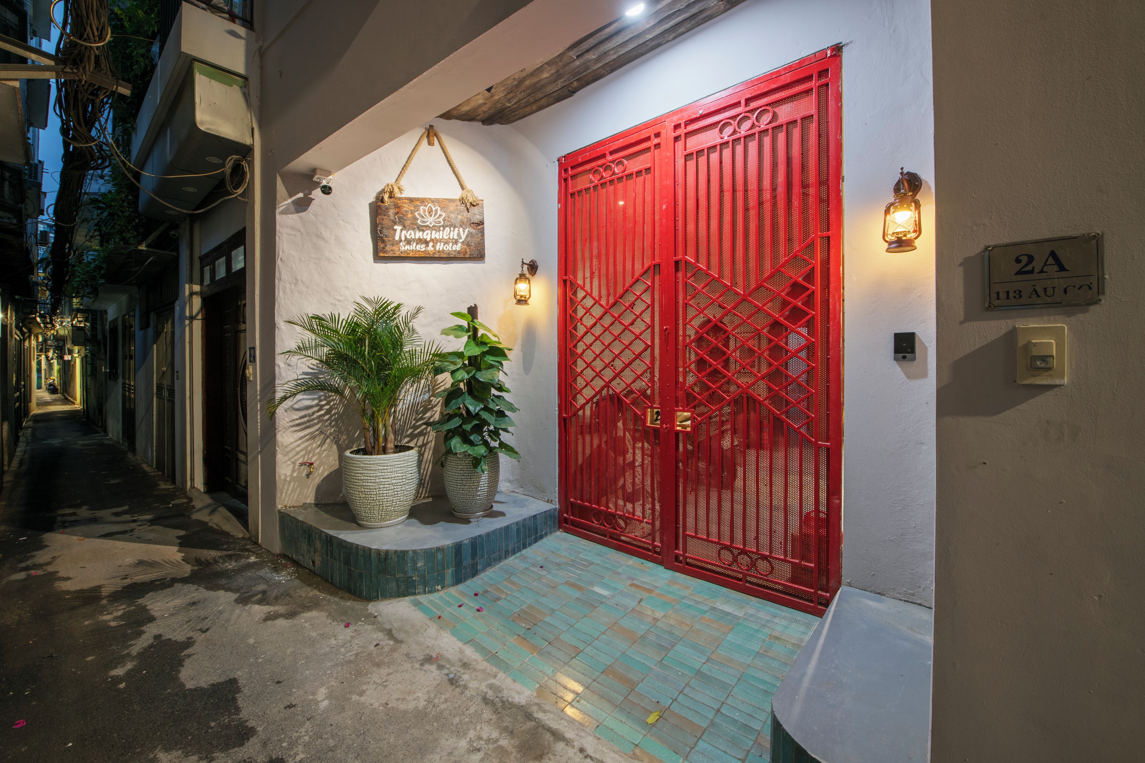 A hotel entrance with a red gate, potted plants, and a sign indicating the name and type of establishment.