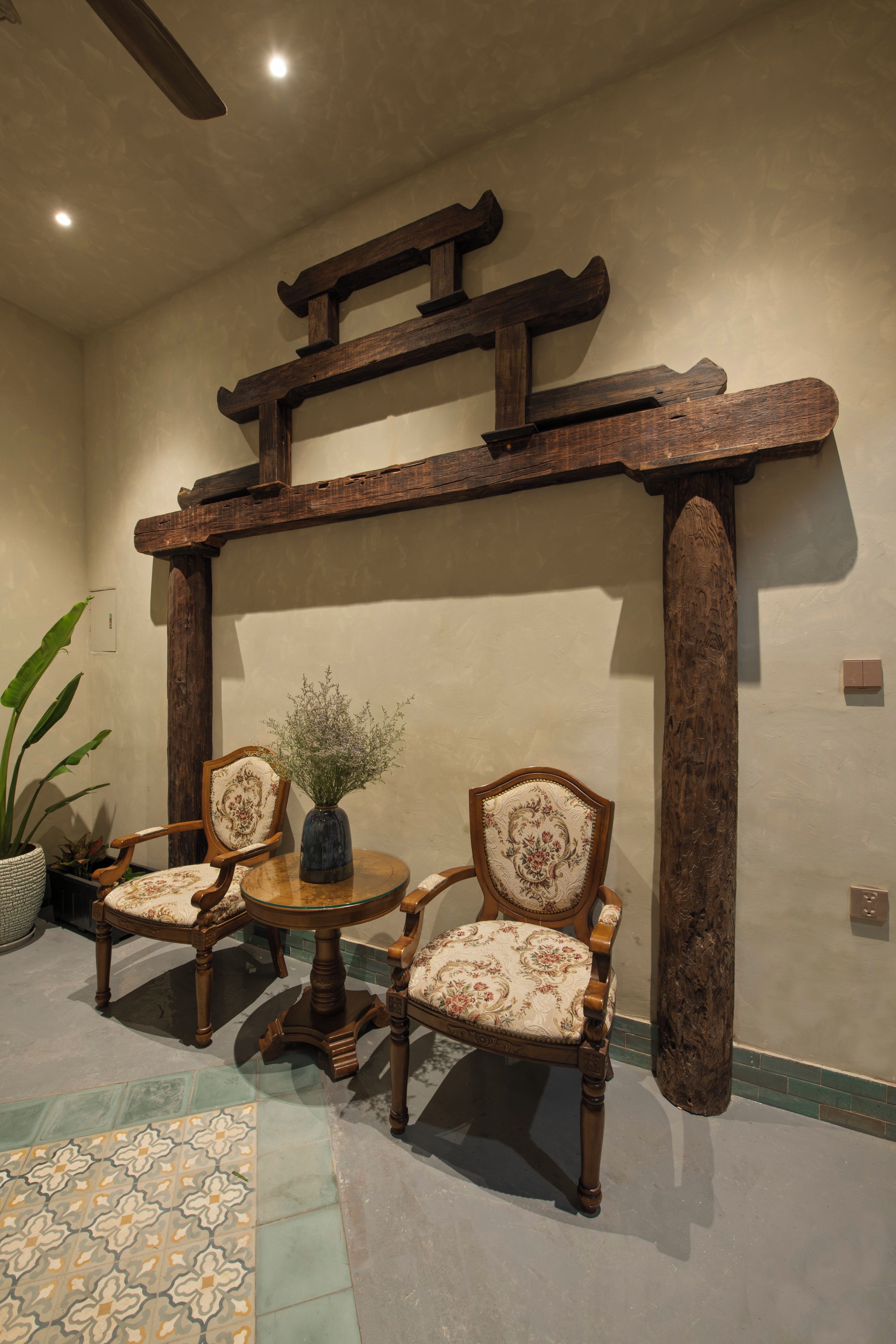 A traditional Japanese interior with a wooden torii gate, two upholstered chairs, a small round table, and a potted plant.