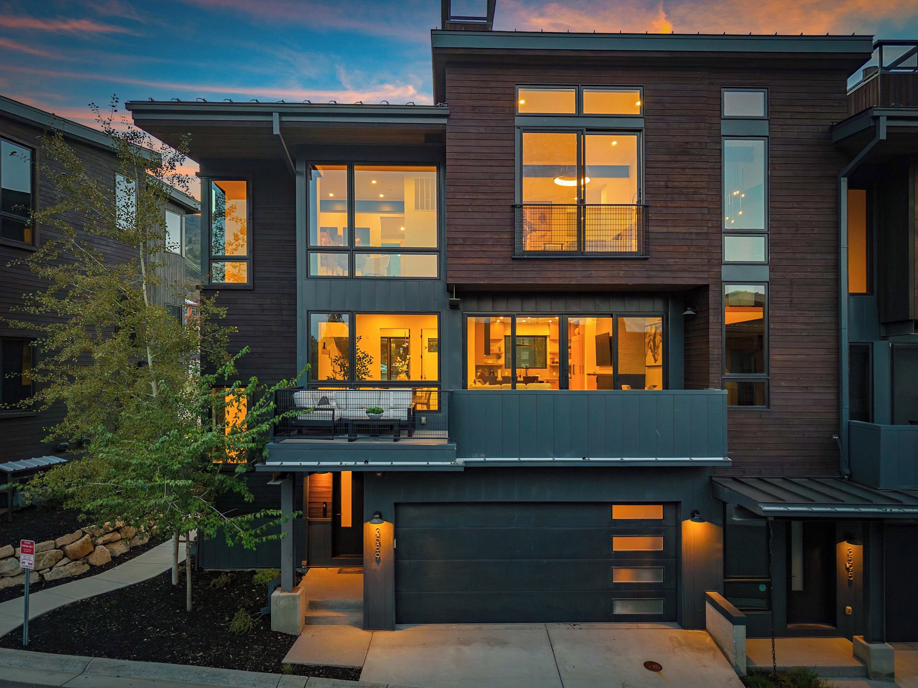 A modern two-story residential building with large windows, a covered porch, and a garage.