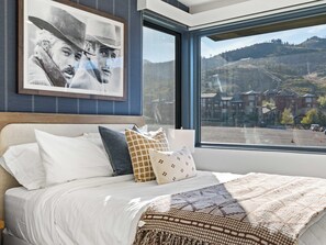A hotel room with a large bed, a view of a ski resort, and a framed picture on the wall. - Ski-In 5BR Canyons Village | Hot Tub + Fire Pit | Steps to Gondola (Park City)