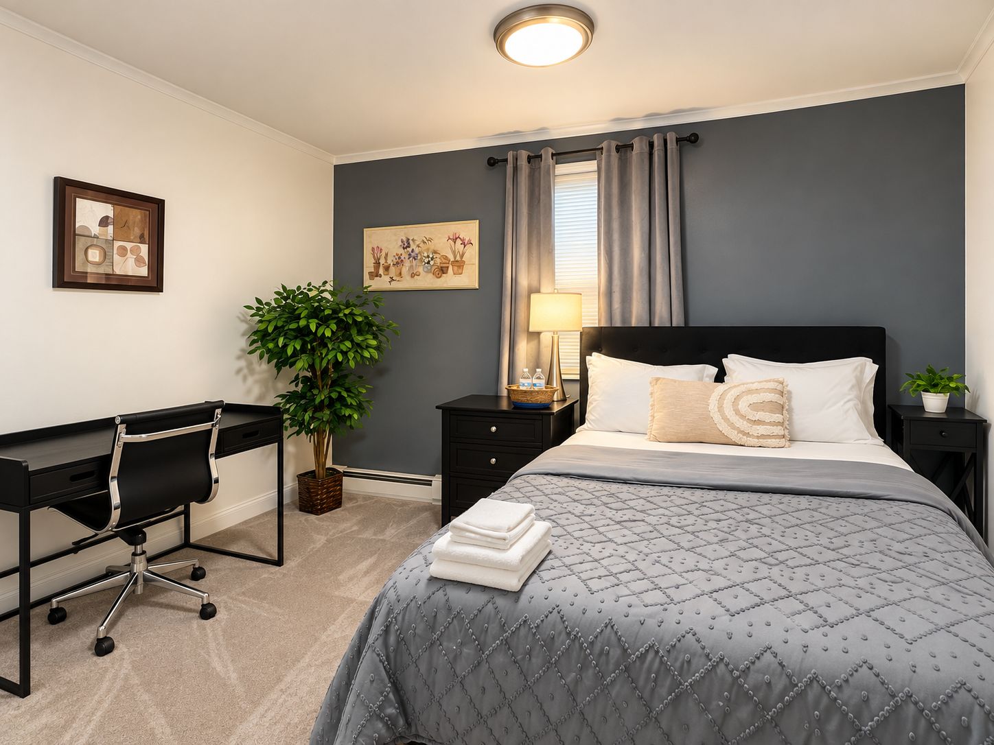 A bedroom with a bed, desk, chair, lamp, and two potted plants.