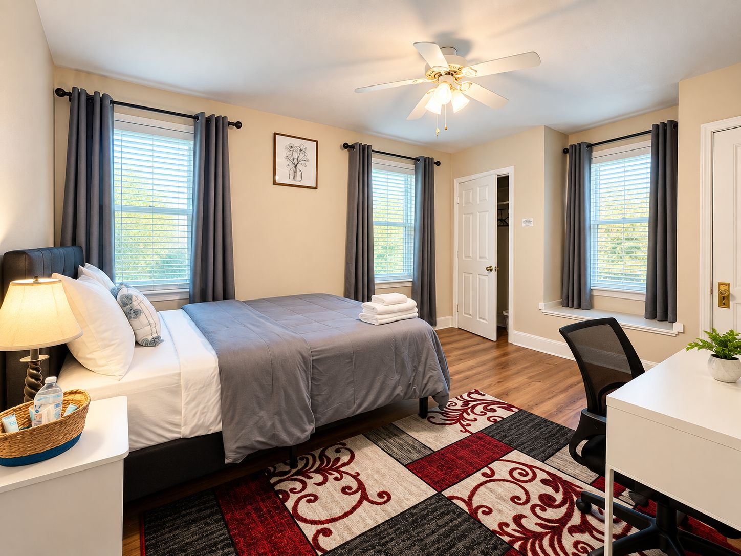 A hotel room with a bed, bedside table, lamp, desk, chair, and a ceiling fan.
