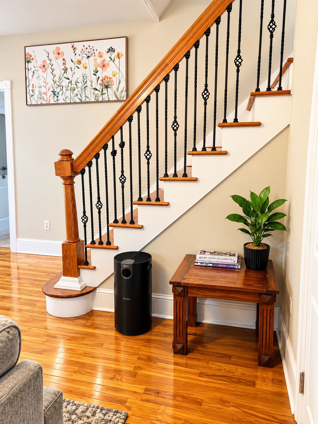 Una escalera con escalones de madera y barandillas negras, una planta en una mesita auxiliar y una obra de arte floral enmarcada en la pared.