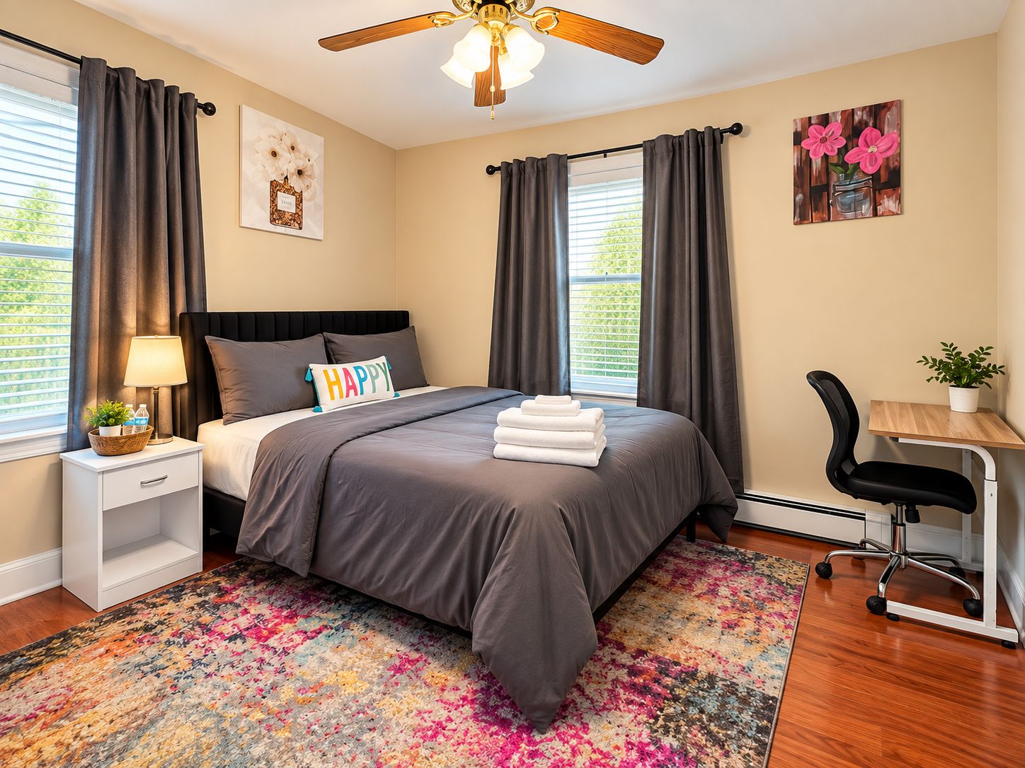A bedroom with a bed, a desk, a chair, a ceiling fan, and a window with curtains.