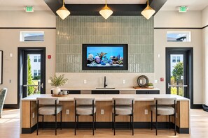A modern kitchen with a large island, bar stools, pendant lighting, and a television mounted above the island. - 1BR King Suite - Pool, Gym, Games & Dog Friendly (Middleburg)