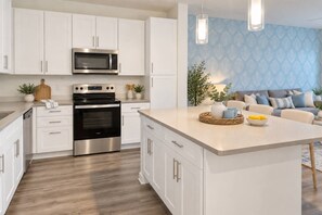 A modern kitchen with white cabinetry, stainless steel appliances, and a central island with a bowl of fruit. - 1BR King Suite - Pool, Gym, Games & Dog Friendly (Middleburg)