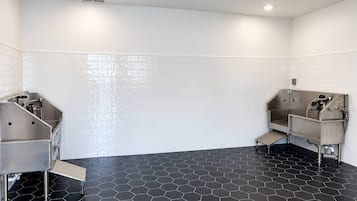 Des toilettes avec deux lavabos, des murs recouverts de carreaux blancs et un sol noir à motifs hexagonaux.
