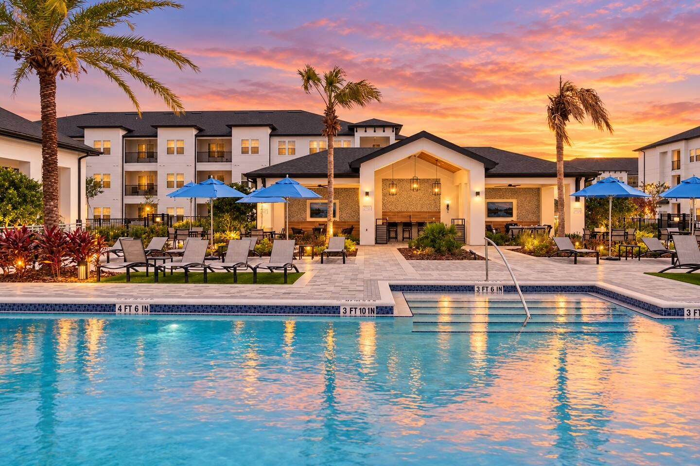 A hotel with a swimming pool, lounge chairs, and umbrellas.