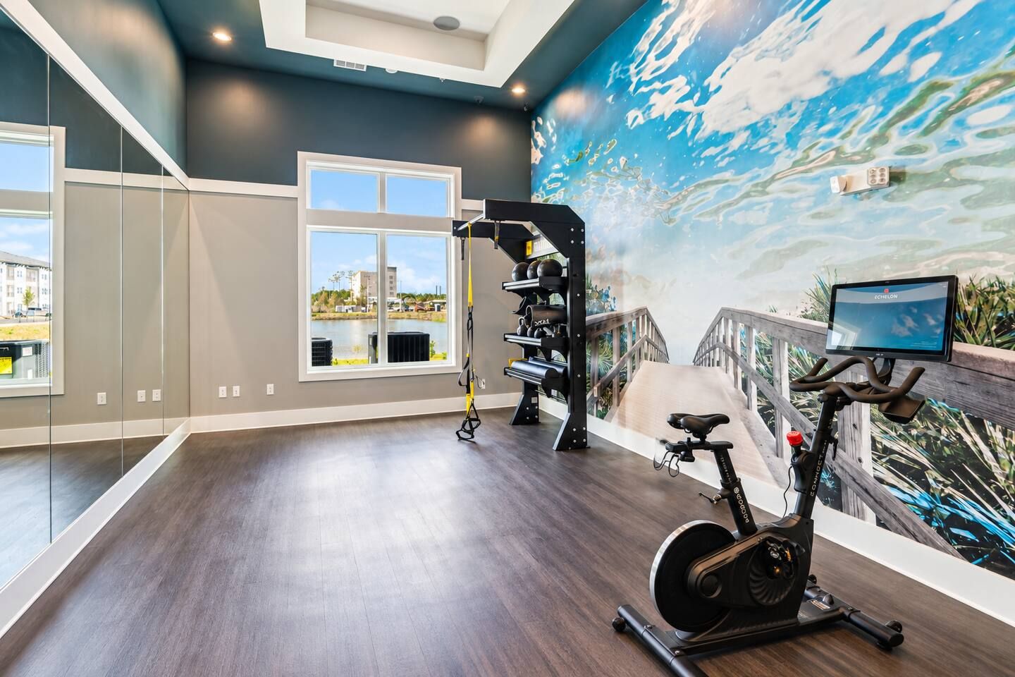 Une salle de sport moderne dotée d’un grand miroir, d’appareils d’exercice et d’une fresque murale représentant un paysage.