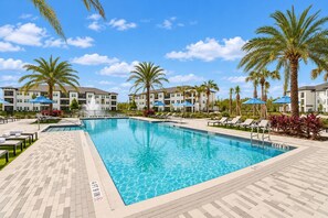A rectangular swimming pool with a tiled edge, surrounded by lounge chairs and palm trees, with a clear sky above. - 2BR Suite - Pool, Gym, Games & Dog Friendly (Middleburg)