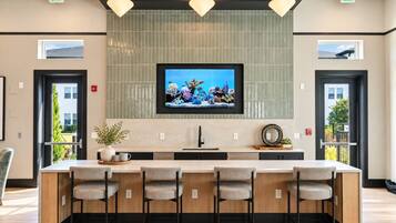 Une cuisine moderne dotée d’un grand îlot central, de tabourets de bar, de luminaires suspendus et d’un téléviseur fixé au-dessus de l’îlot.