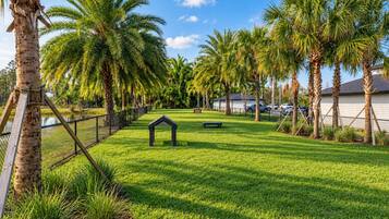 A well-maintained grassy area with palm trees, a small gazebo, and a fence.