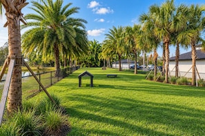 A well-maintained grassy area with palm trees, a small gazebo, and a fence. - 2BR Suite - Pool, Gym, Games & Dog Friendly (Middleburg)