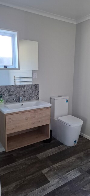 A bathroom with a white sink, a mirror, a toilet, and a trash bin. - Coastal getaway in beautiful Kaikoura (Kaikōura)