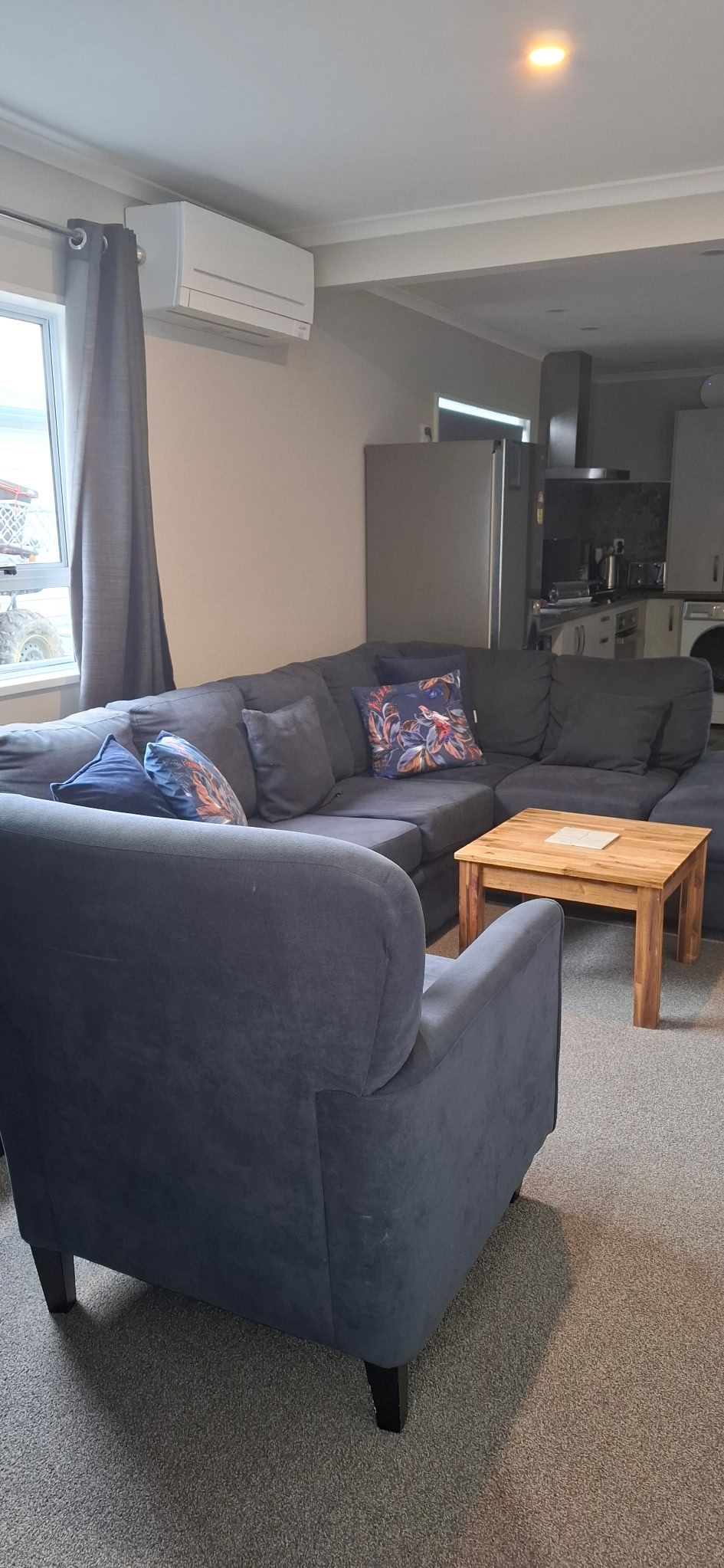 A modern living room with a grey sofa, a wooden coffee table, and a kitchen in the background.