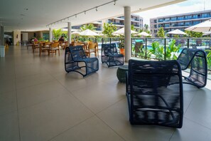 Un espacio interior amplio con arreglos de asientos, una piscina visible a través del vidrio y un edificio moderno al fondo.