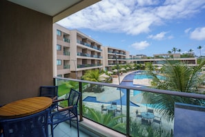 Un balcon avec une table et des chaises, donnant sur une piscine et un immeuble doté de nombreux balcons.