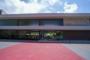 Un bâtiment moderne doté de grandes fenêtres et d’un chemin d’accès en briques rouges menant à l’entrée.