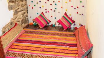 A cozy room with a stone wall, a colorful woven rug, and a wall hanging with colorful pom-poms.