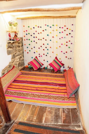 A cozy room with a stone wall, a colorful woven rug, and a wall hanging with colorful pom-poms.