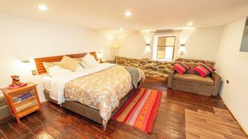 A bedroom with a bed, a nightstand, a sofa, and a stone wall.