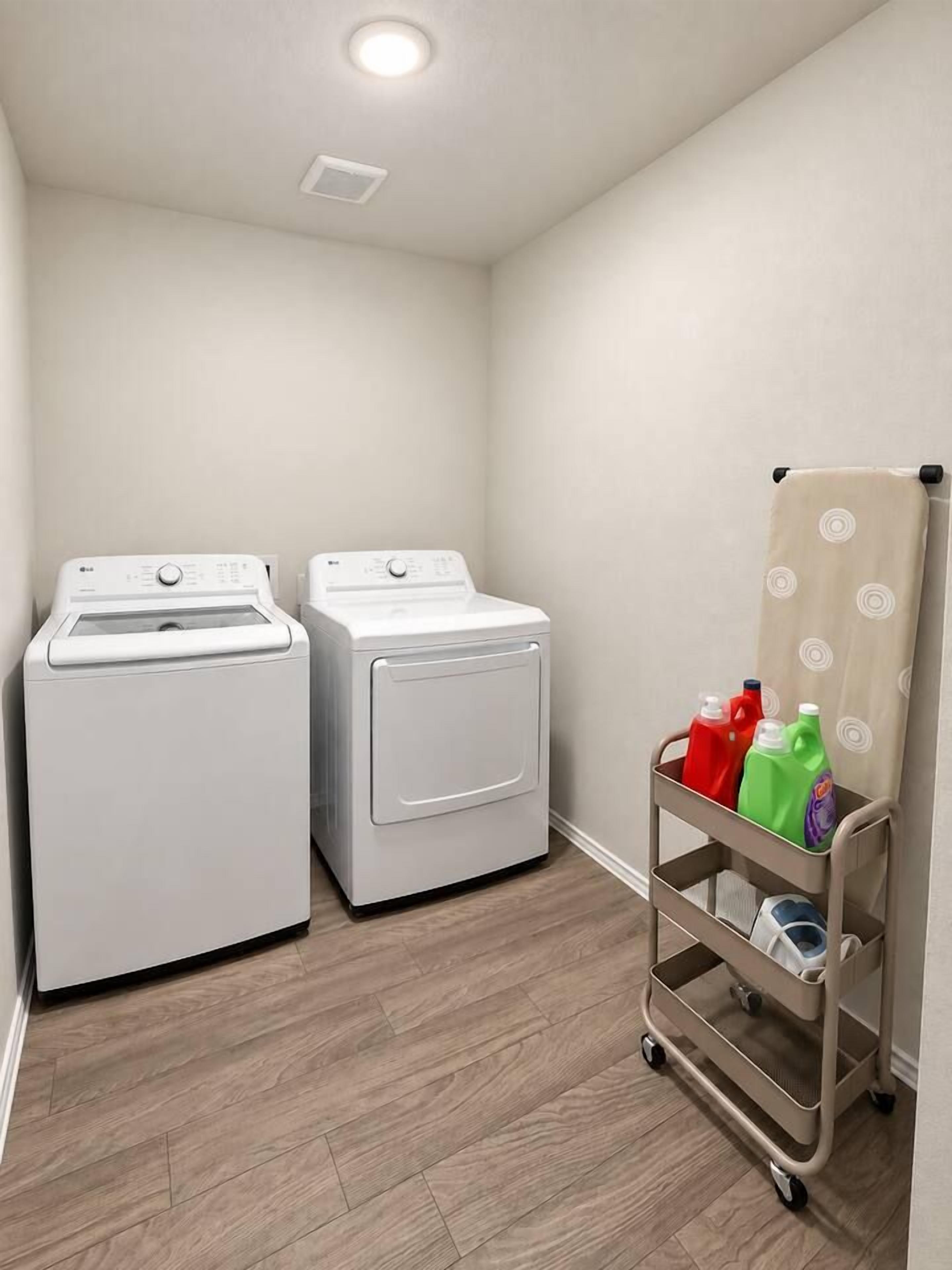 A laundry room with two white front-loading washing machines, a cart with detergent bottles, and a wooden floor.