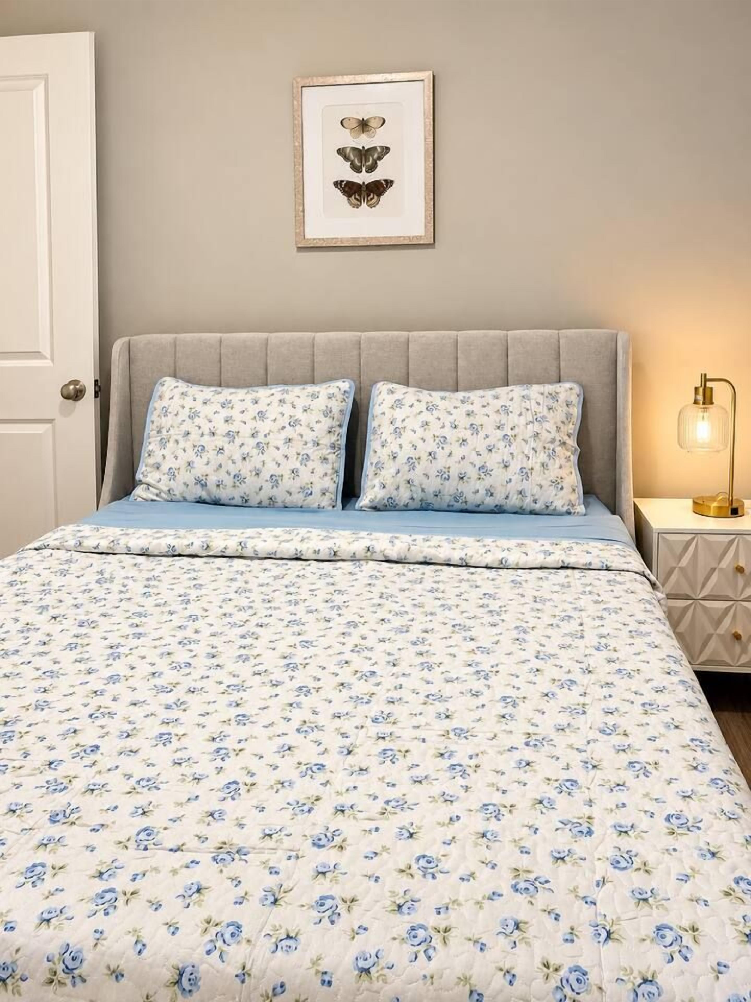 Quarto com cama, duas almofadas, mesa de cabeceira e moldura na parede.