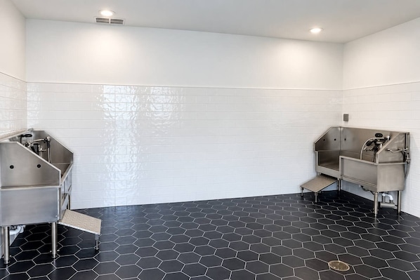 A restroom with two sinks, white tiled walls, and a black hexagonal floor. - 2BR Suite - Pool, Gym, Games & Dog Friendly (Middleburg)