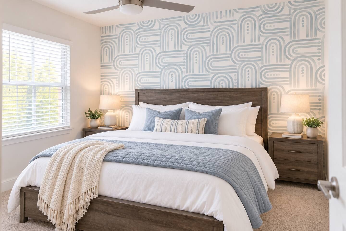 A bedroom with a bed, nightstands, a ceiling fan, and patterned wallpaper.