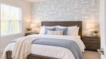 A bedroom with a bed, nightstands, a ceiling fan, and patterned wallpaper.