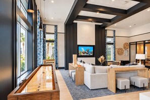 Ein modernes Wohnzimmer mit Billardtisch, großem Flachbildfernseher und einer Sitzecke mit Sofas und Poufs.