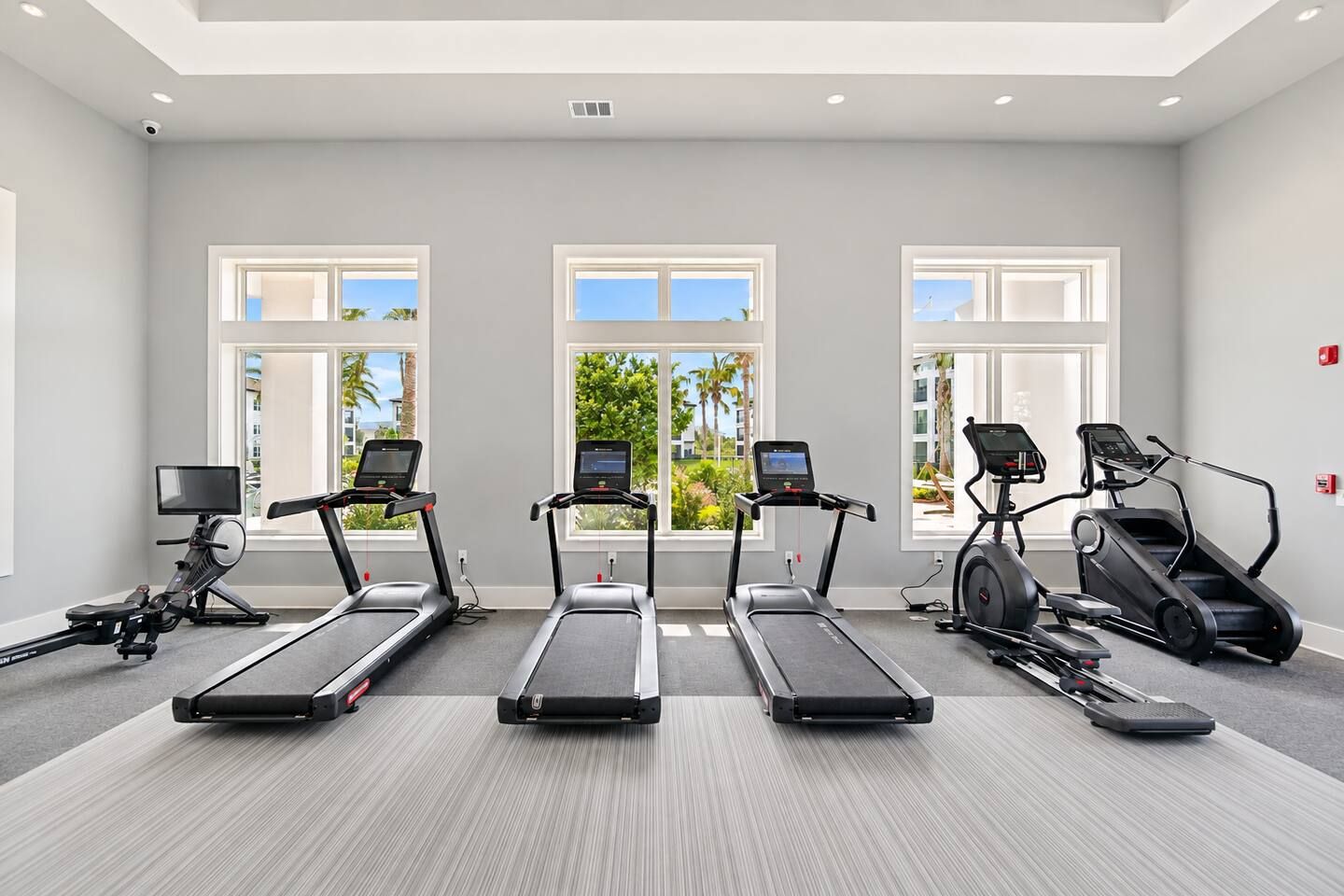 A gym with three treadmills, one elliptical, and a stationary bike, all with digital screens.