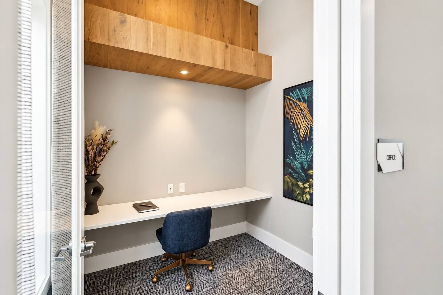 A modern office space with a wooden ceiling, a white desk, a blue office chair, and a wall-mounted picture.
