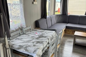 A room with a sofa, a table, and a window with curtains. - 6Berth Caravan-Wheelchair Accessible-Pet Friendly (Skegness)