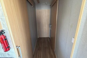 A narrow hallway with wooden walls and a wooden floor, leading to a door. A red fire extinguisher is mounted on the wall to the left. - 6Berth Caravan-Wheelchair Accessible-Pet Friendly (Skegness)
