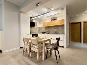 Een moderne keuken met een eethoek, met een houten tafel en stoelen, een inbouwoven en een klok aan de muur.