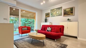 En moderne stue med en rød sofa, et sofabord og et stort vindue med persienner.