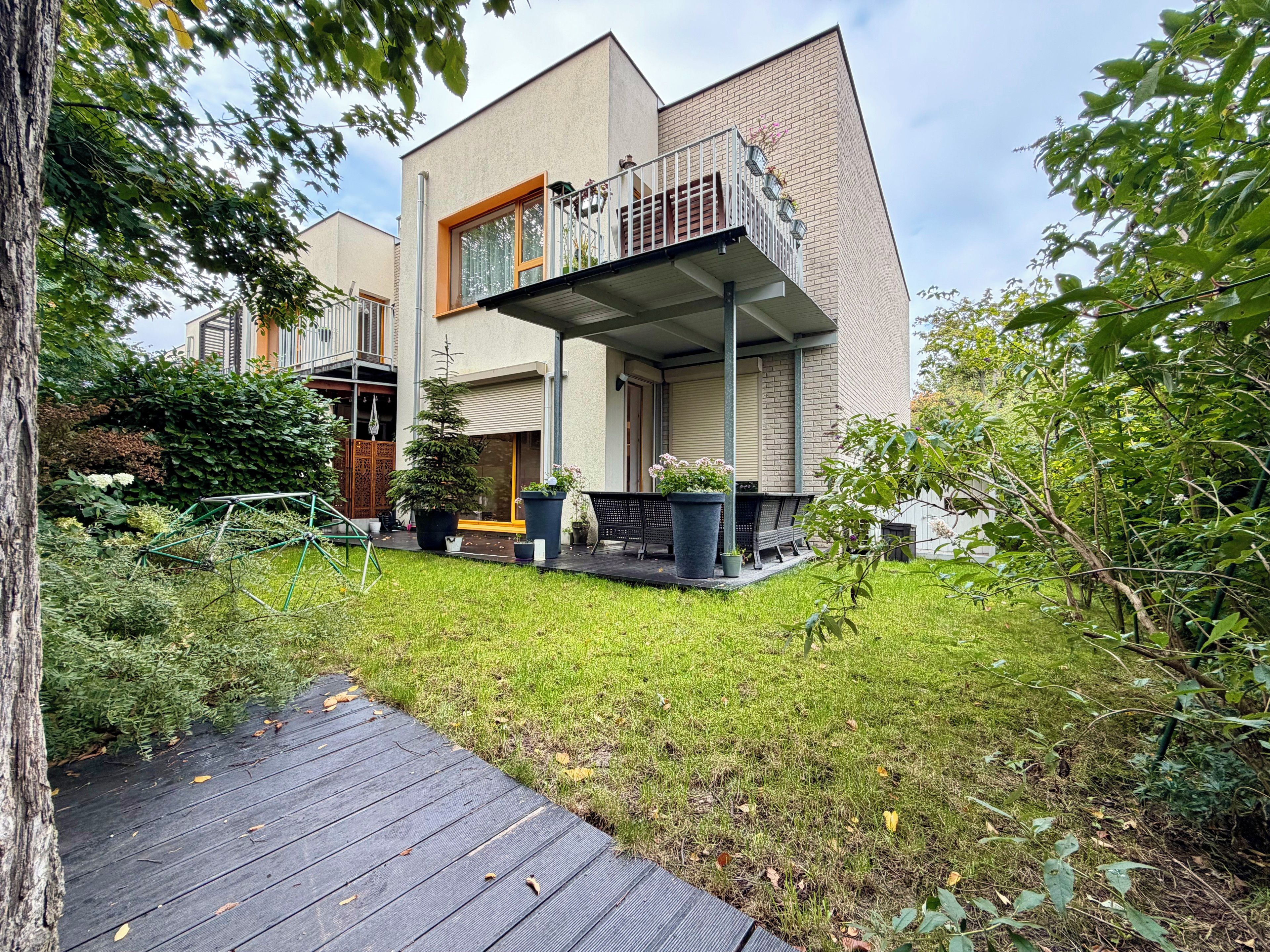 Een modern huis met een balkon, een houten terras en een tuin.