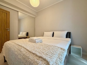 Een slaapkamer met een bed, nachtkastje, spiegel en kledingkast.