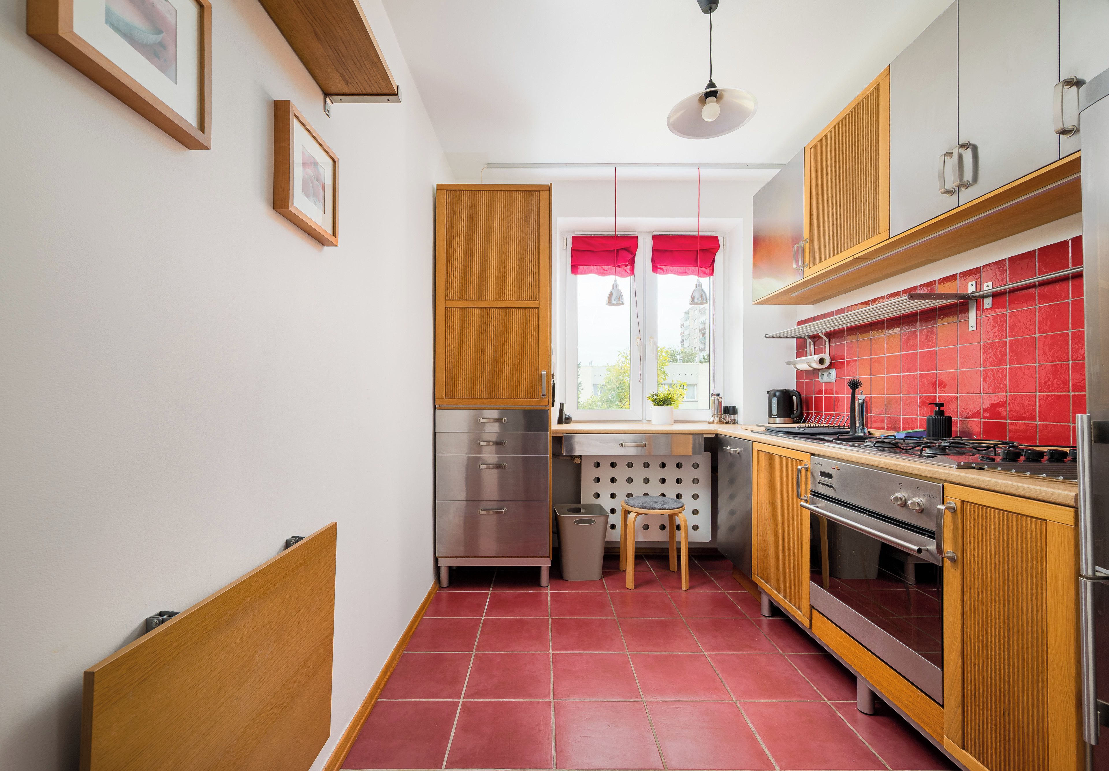 A compact kitchen with wooden cabinets, a stainless steel stove, and a red tiled backsplash.