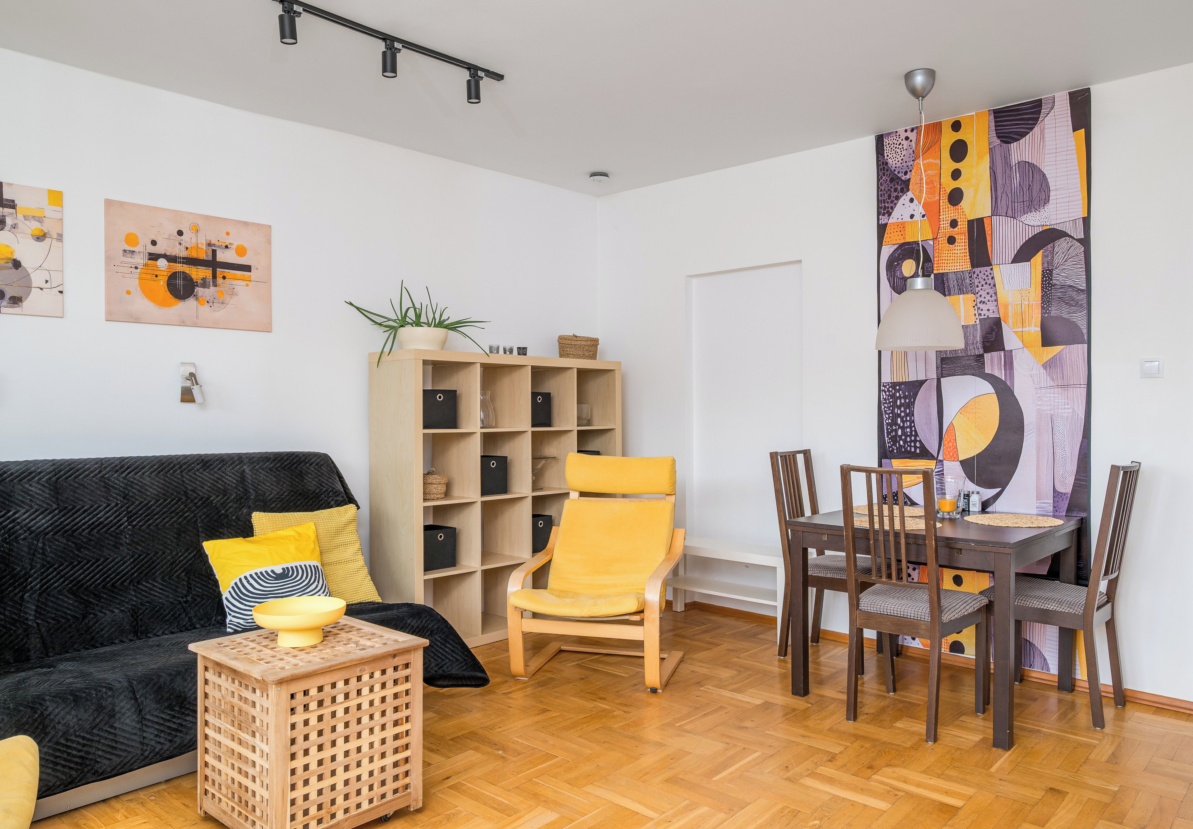 Ein Wohnzimmer mit einer Couch, einem Couchtisch, einem Bücherregal, einem Esstisch mit Stühlen und abstrakter Wandkunst.