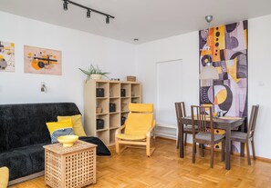 Un salon comprenant un canapé, une table basse, une bibliothèque, une table à manger avec des chaises et des œuvres d’art abstraites accrochées au mur.