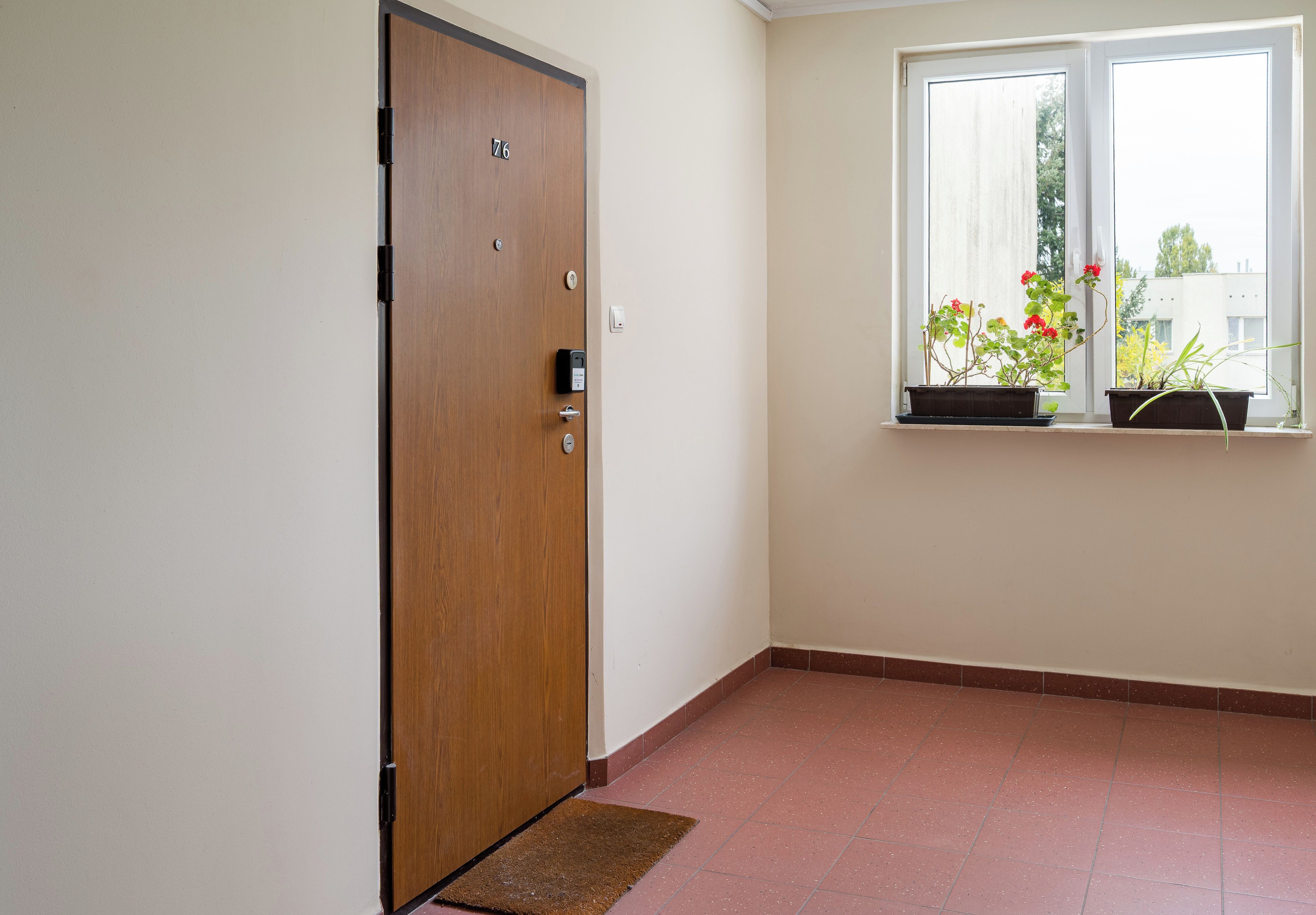 Ein Zimmer mit Holztür, einem Fenster mit Blumentöpfen und einem Fliesenboden.