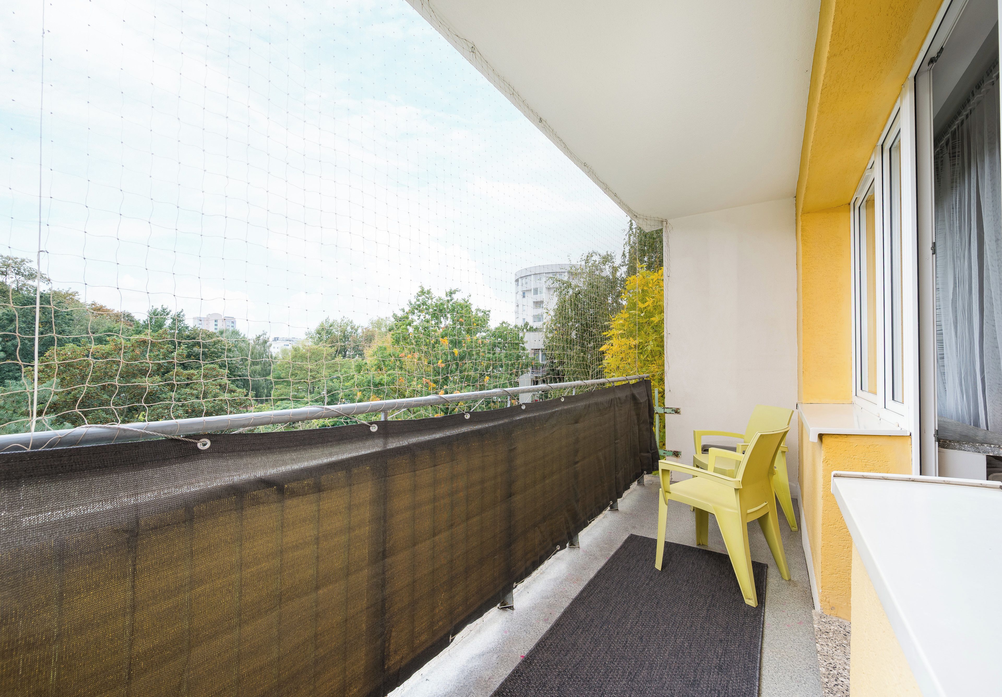 Un balcone con un muro giallo, una ringhiera in rete nera e due sedie gialle.